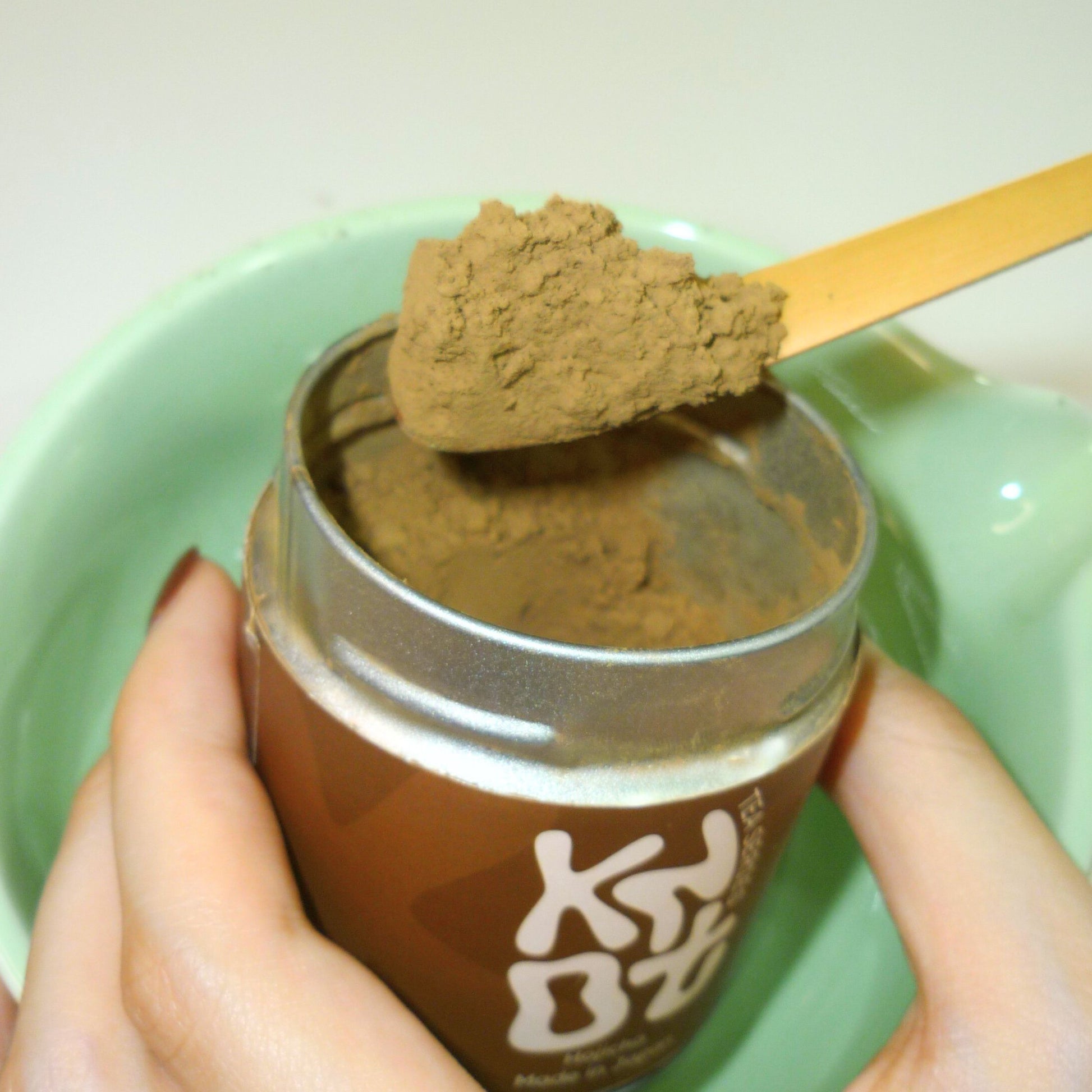 Tin of hojicha powder with a wooden scoop in a green chawan
